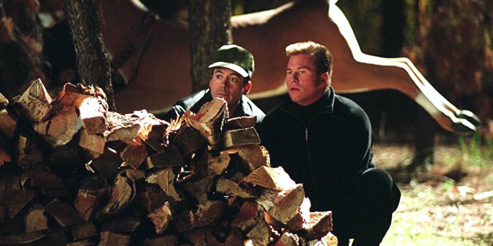 Roberto Downey Jr.  e Val Kilmer se escondendo atrás de uma pilha de árvores do lado de fora em Kiss, Kiss, Bang, Bang