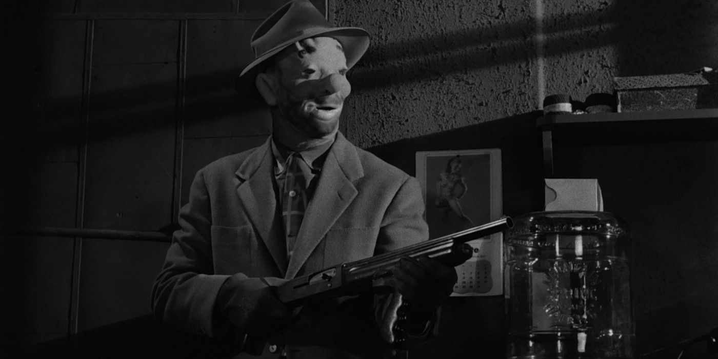 A man in a clown mask aiming a gun ahead in The Killing (1956)