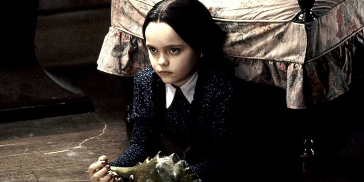 Christina Ricci interpreta Wednesday Addams com um dinossauro de brinquedo no filme A Família Addams