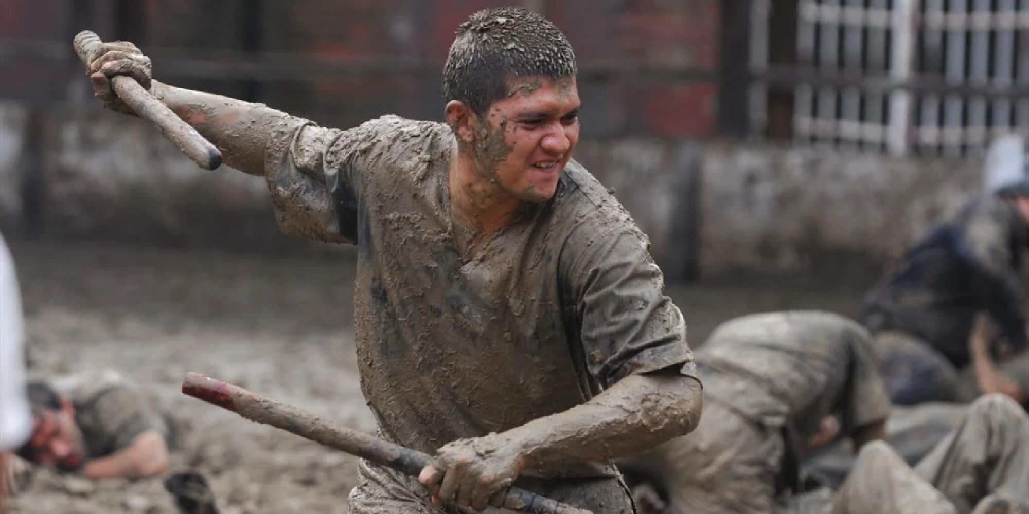 A young man wielding two sticks while covered in mud in The Raid 2.