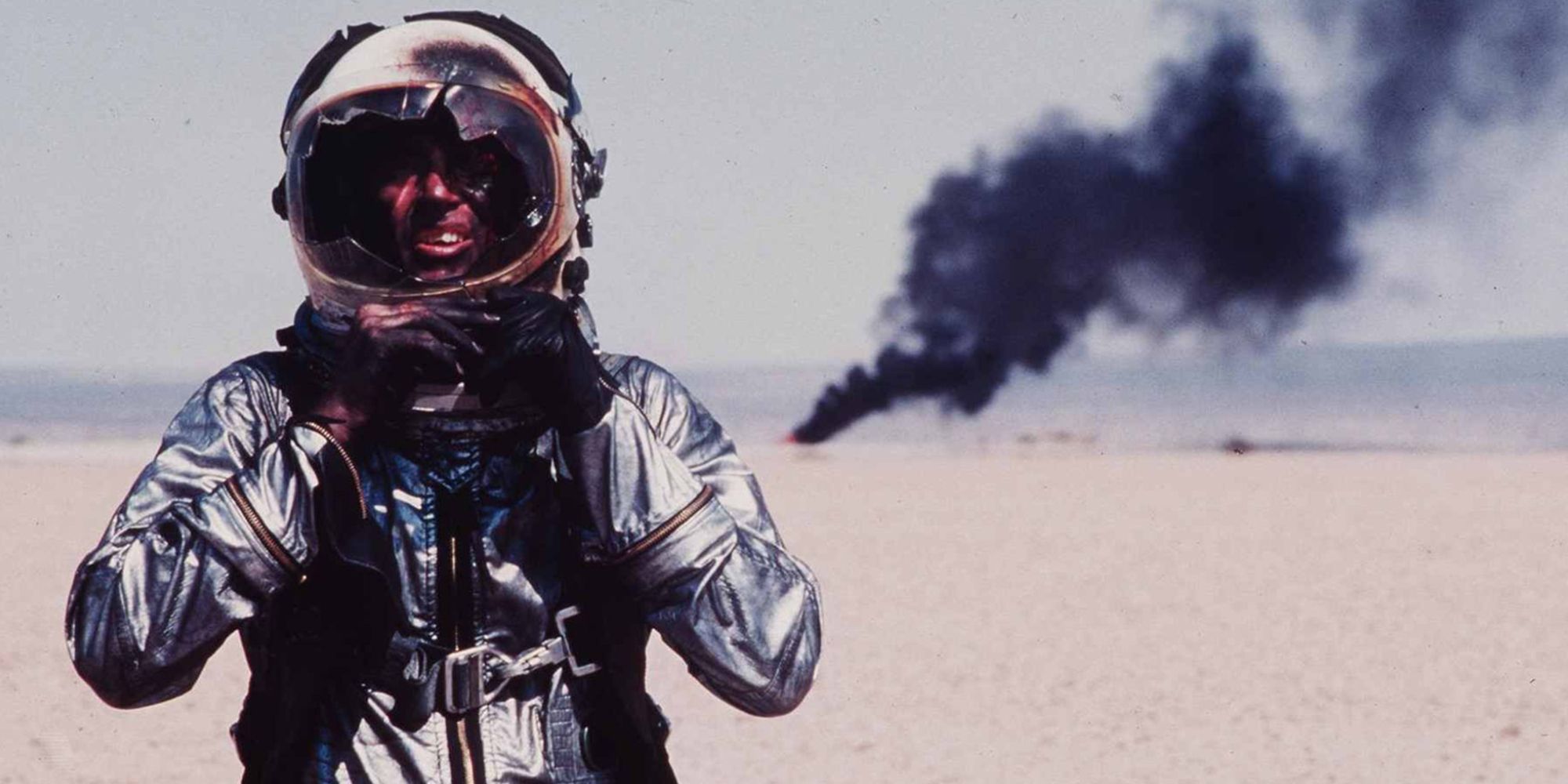 A battered astronaut stands while, in the background, his shuttle burns. 