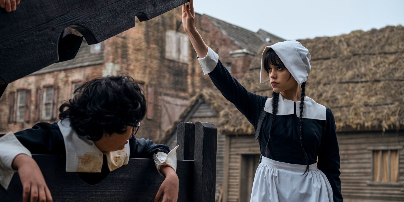 Wednesday, played by Jenna Ortega, dressed in a pilgrim costume, frees a similarly costumed Eugene, played by Moosa Mostafa, from a wooden pillory at Pilgrim World in Netflix's 'Wednesday.'