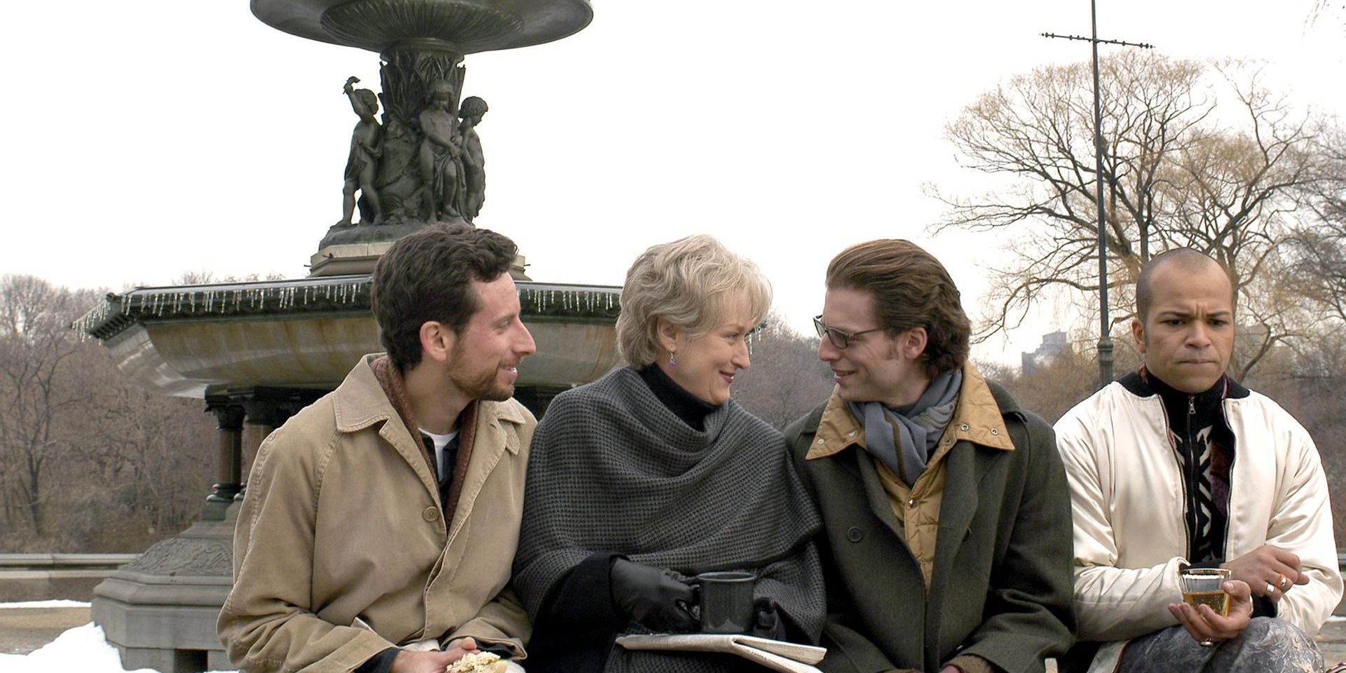Three men talking to a woman in front of a fountain in 