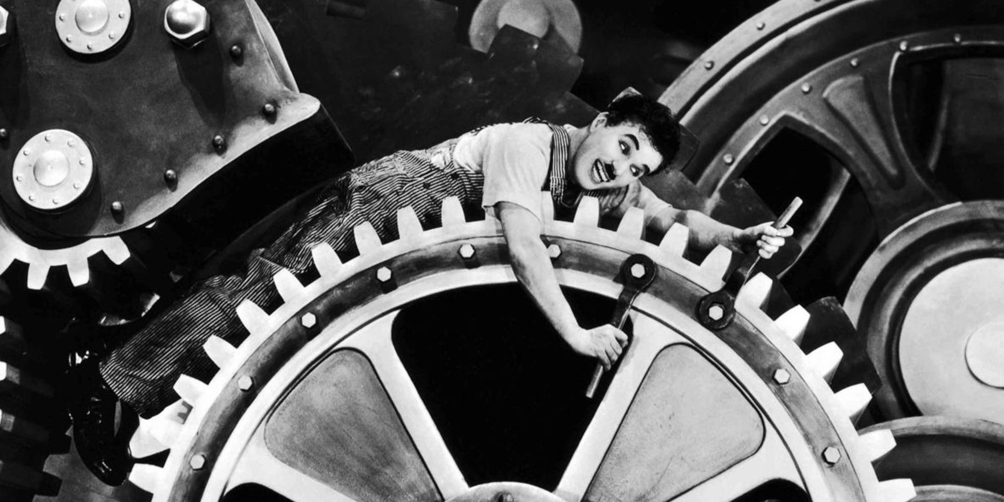 Charlie Chaplin as a factory worker smiling while lying on a giant cogwheel in 'Modern Times'