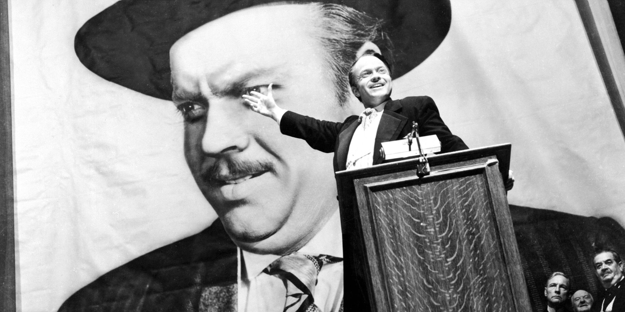 Orson Welles as Charles Foster Kane standing infront of a banner of himself in Citizen Kane