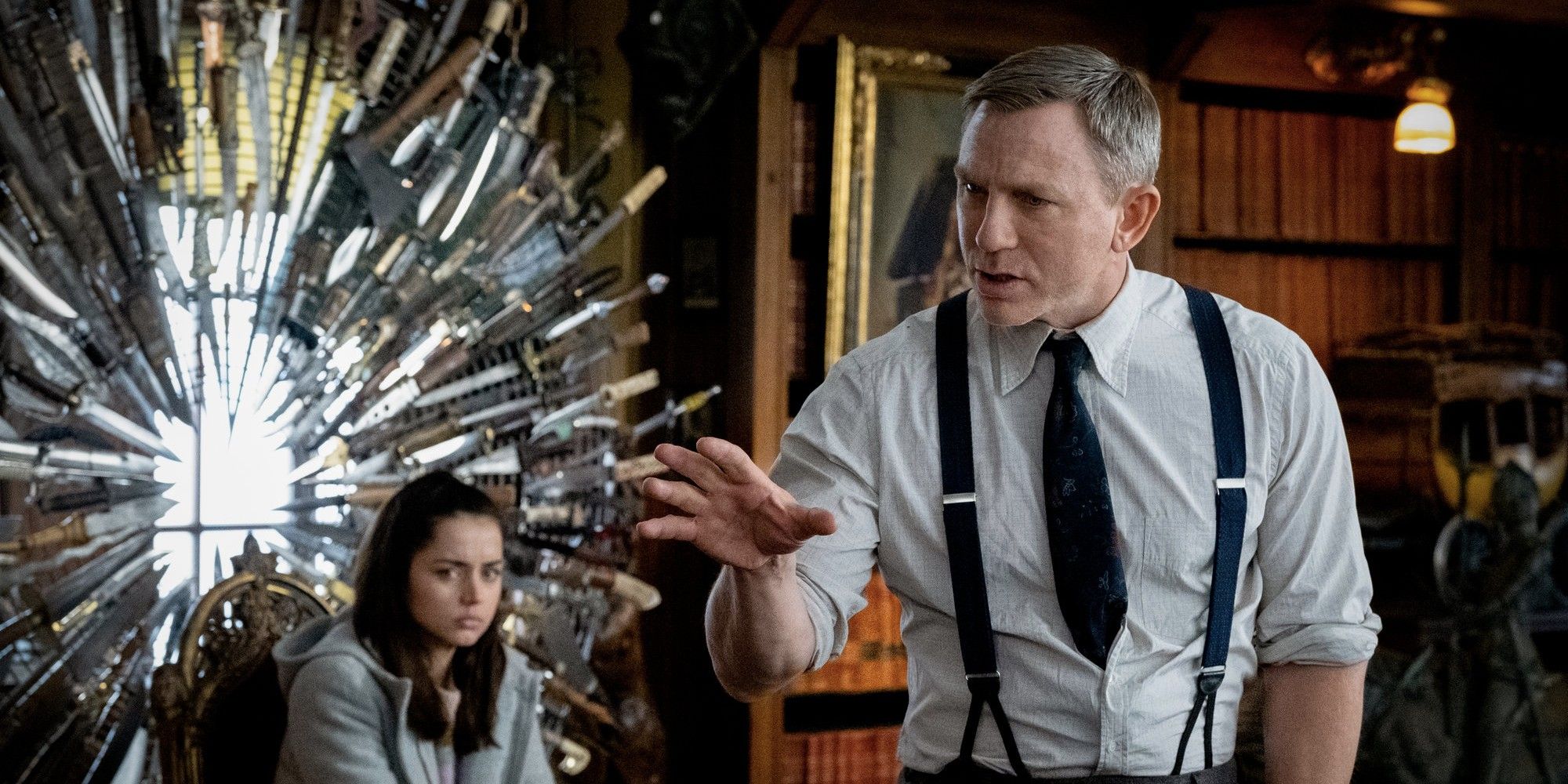 Daniel Craig talking with his hands while Ana de Armas looks at him in the background in 'Knives Out.'