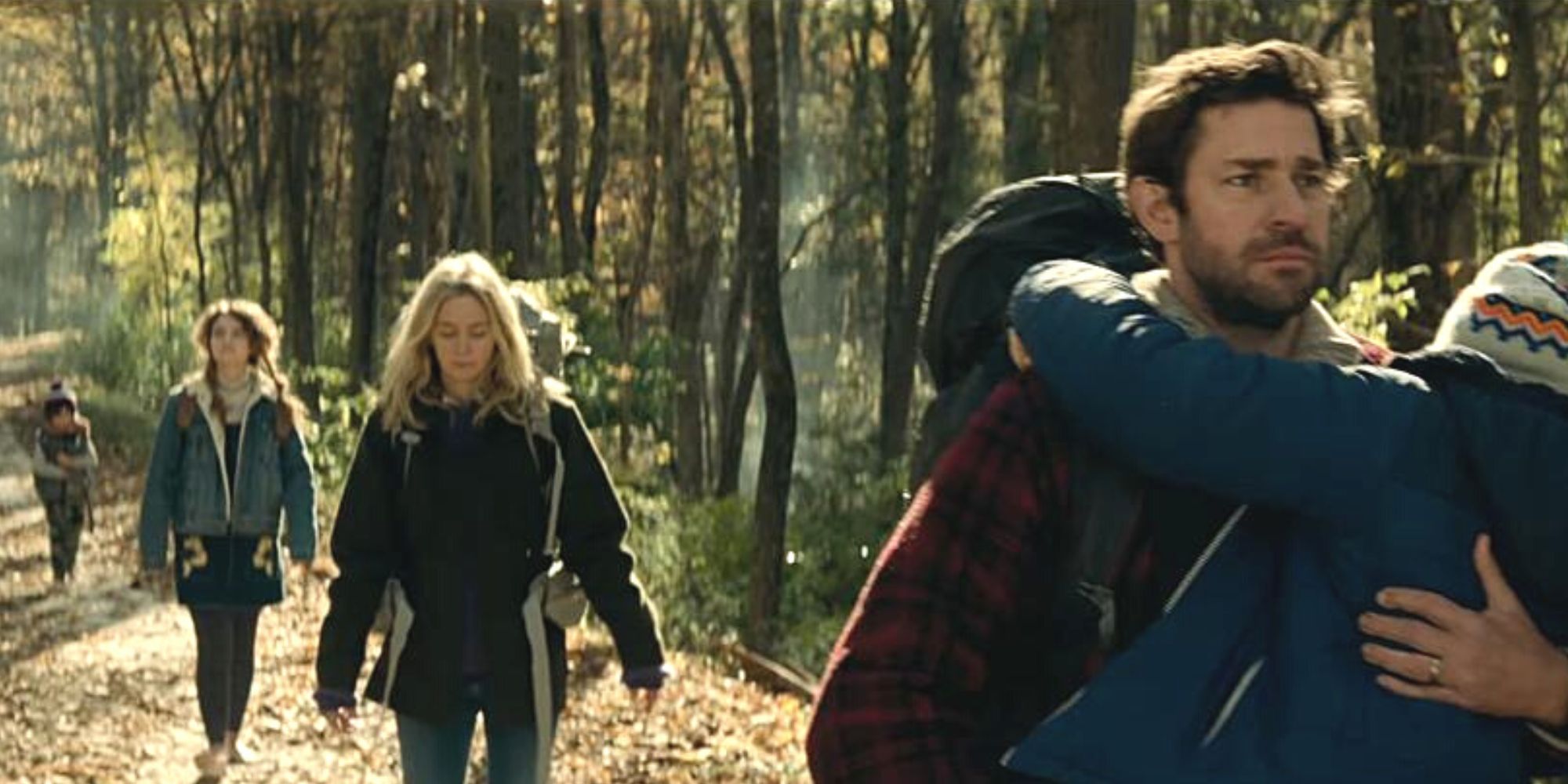 Emily Blunt follows John Krasinski holding a boy while walking in the woods in A Quiet Place