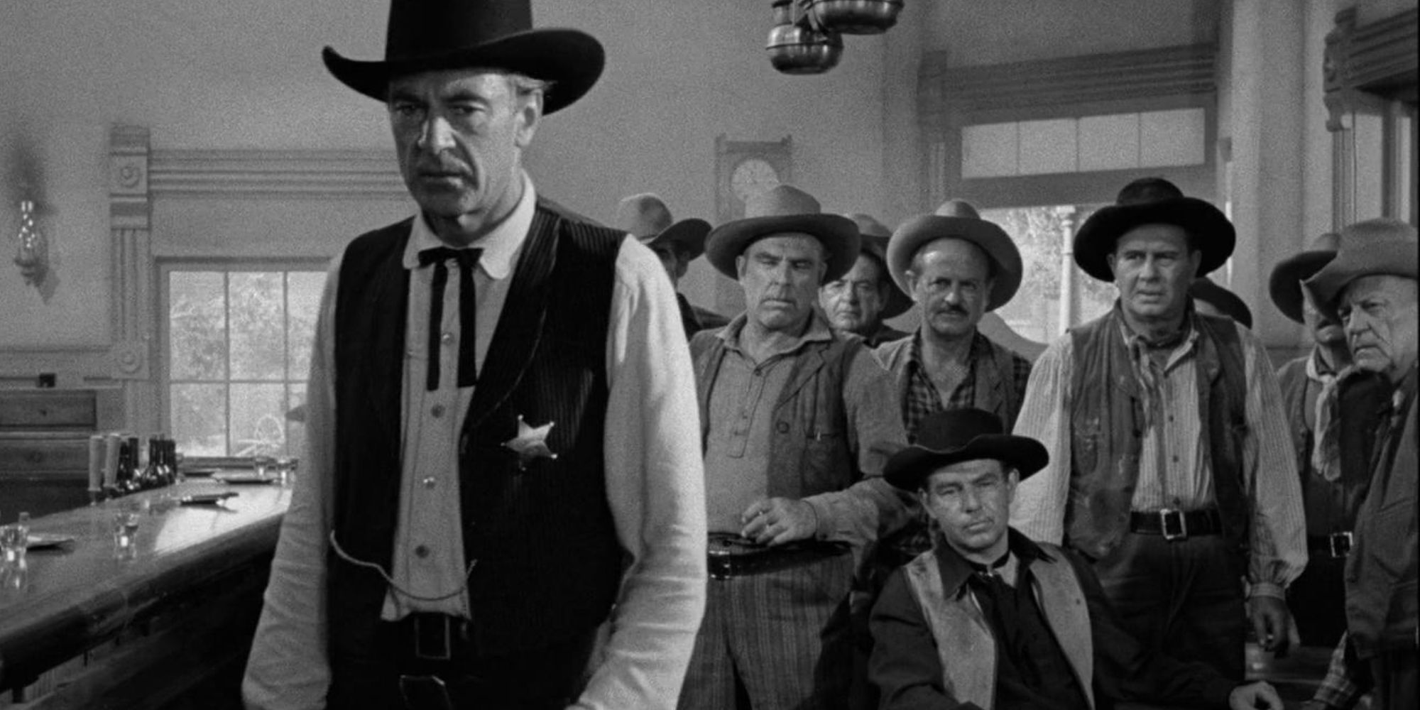 Gary Cooper standing in a saloon with a group of men behind him in High Noon