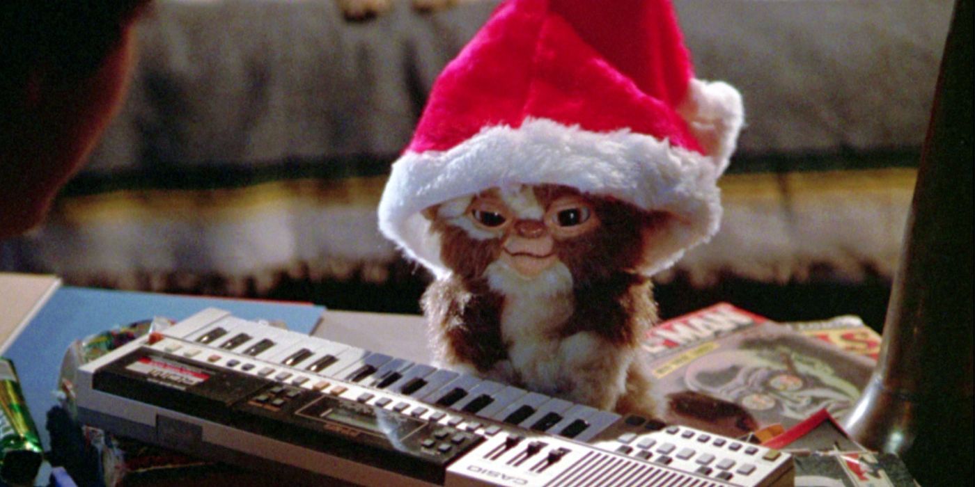 Gizmo standing in front of a keyboard wearing a Santa hat in Gremlins