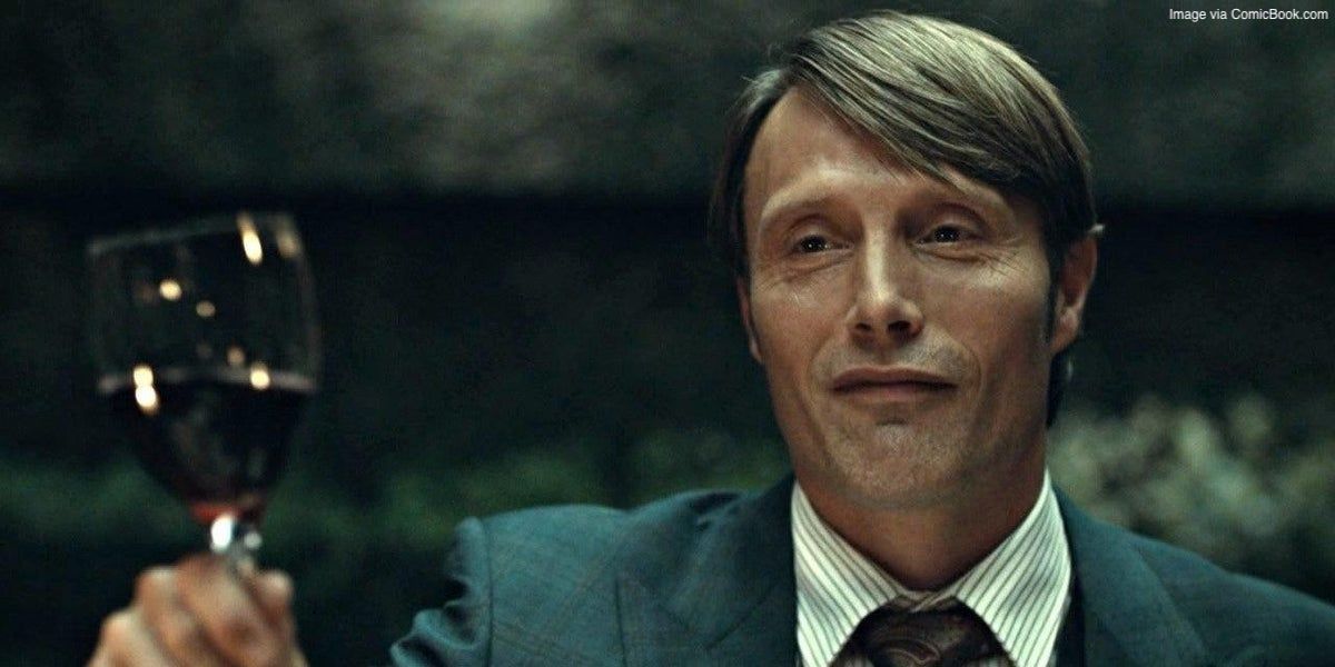 Hannibal Lecter de Hannibal tenant un verre de vin rouge avec un air suffisant sur son visage.