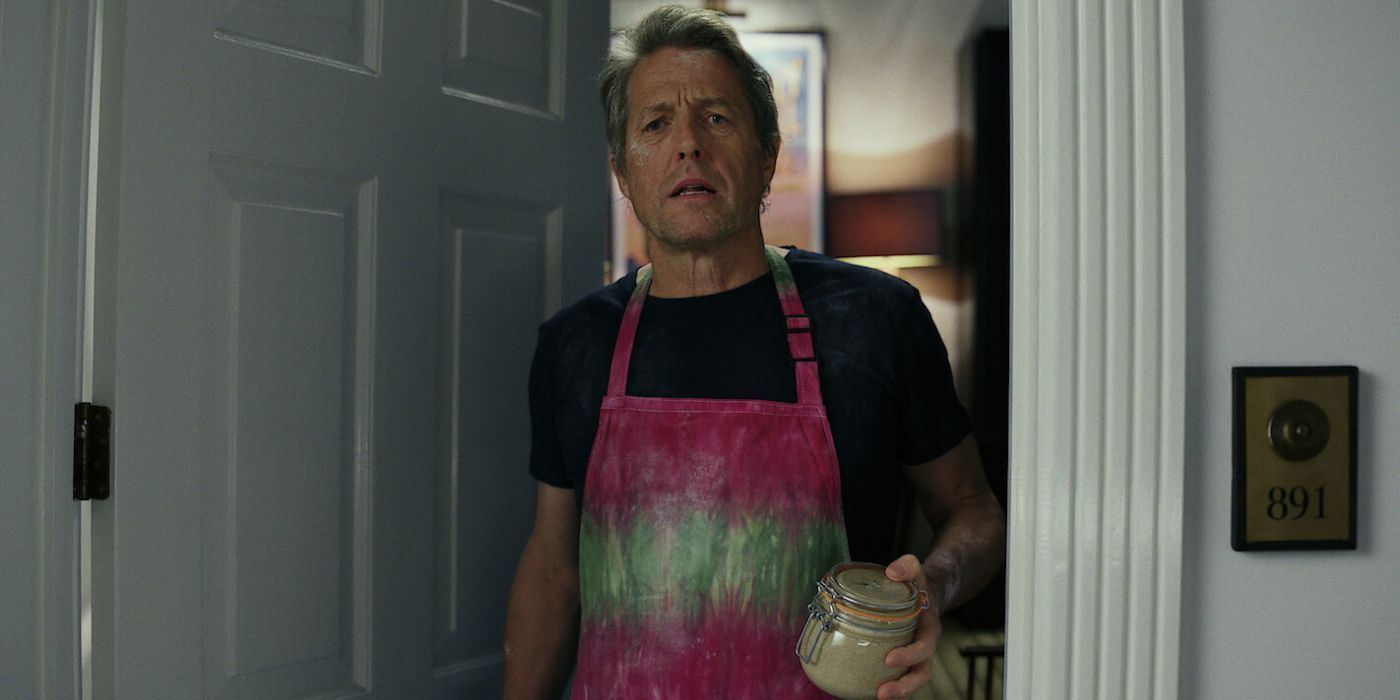 Hugh Grant wearing an apron and holding a jar in the Glass Onion: A Knives Out Mystery