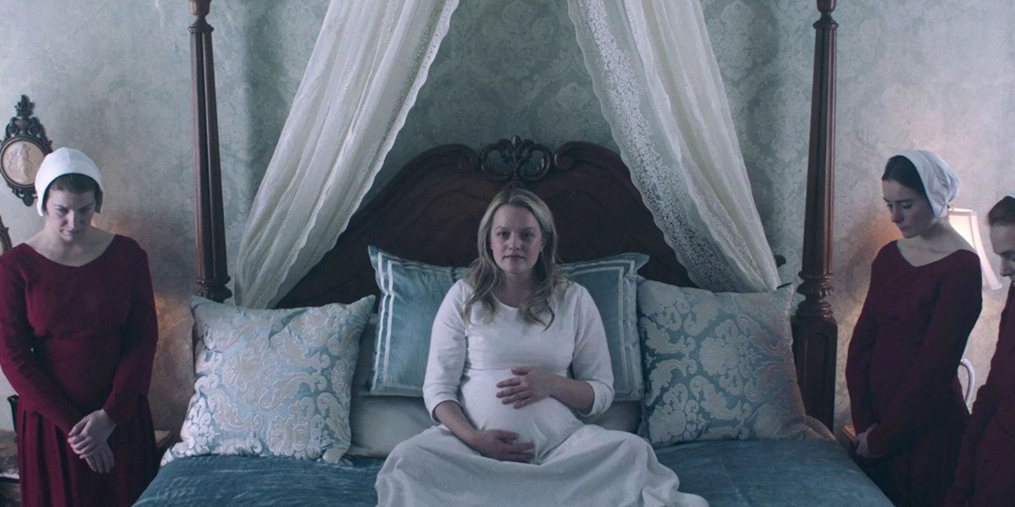 Une Offred enceinte assise sur un lit, entourée de servantes.