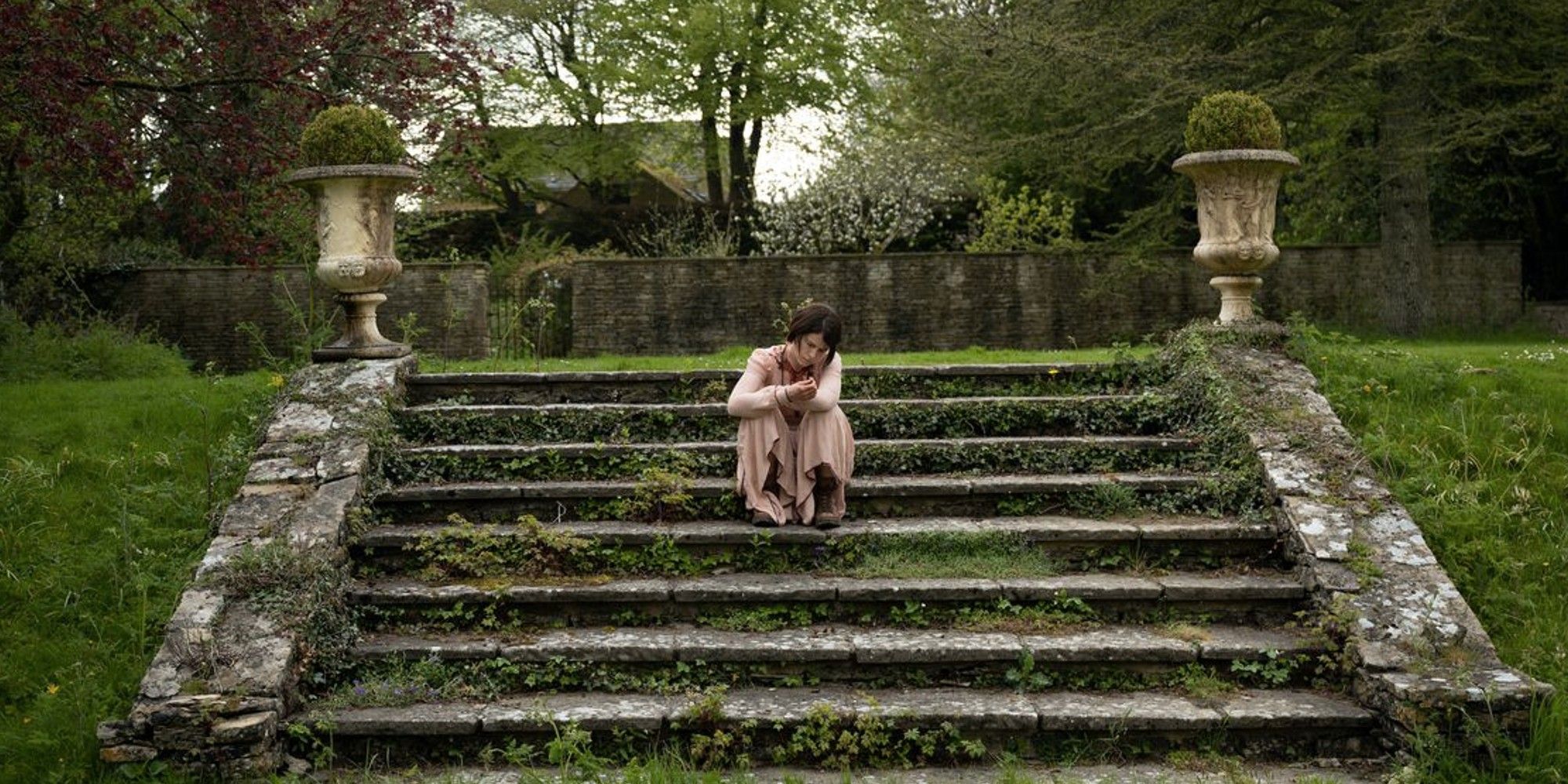 Jessie Buckley sitting on stairs in 'Men'