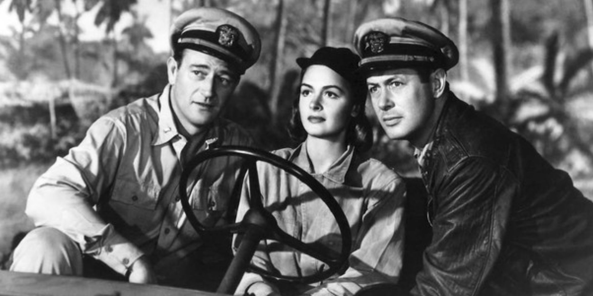 John Wayne, Geraldine Page and Robert Montgomery sitting next to each other in a jeep inThey Were Expendable 