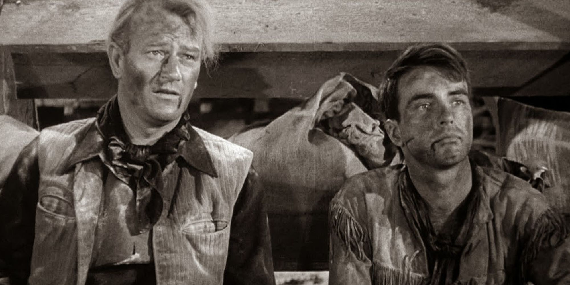 John Wayne e Montgomery Clift sentados um ao lado do outro no chão, olhando para frente em Red River