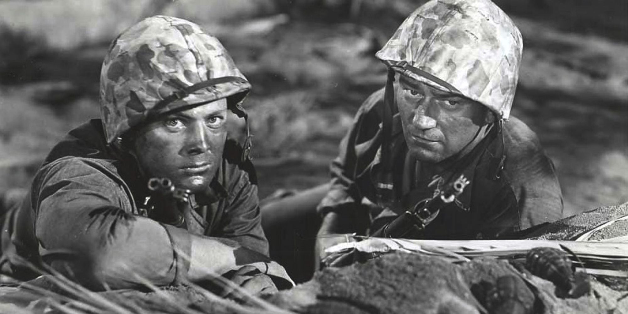 John Wayne lying on the ground of a battle field next to another soldier in Sands of Iwo Jima