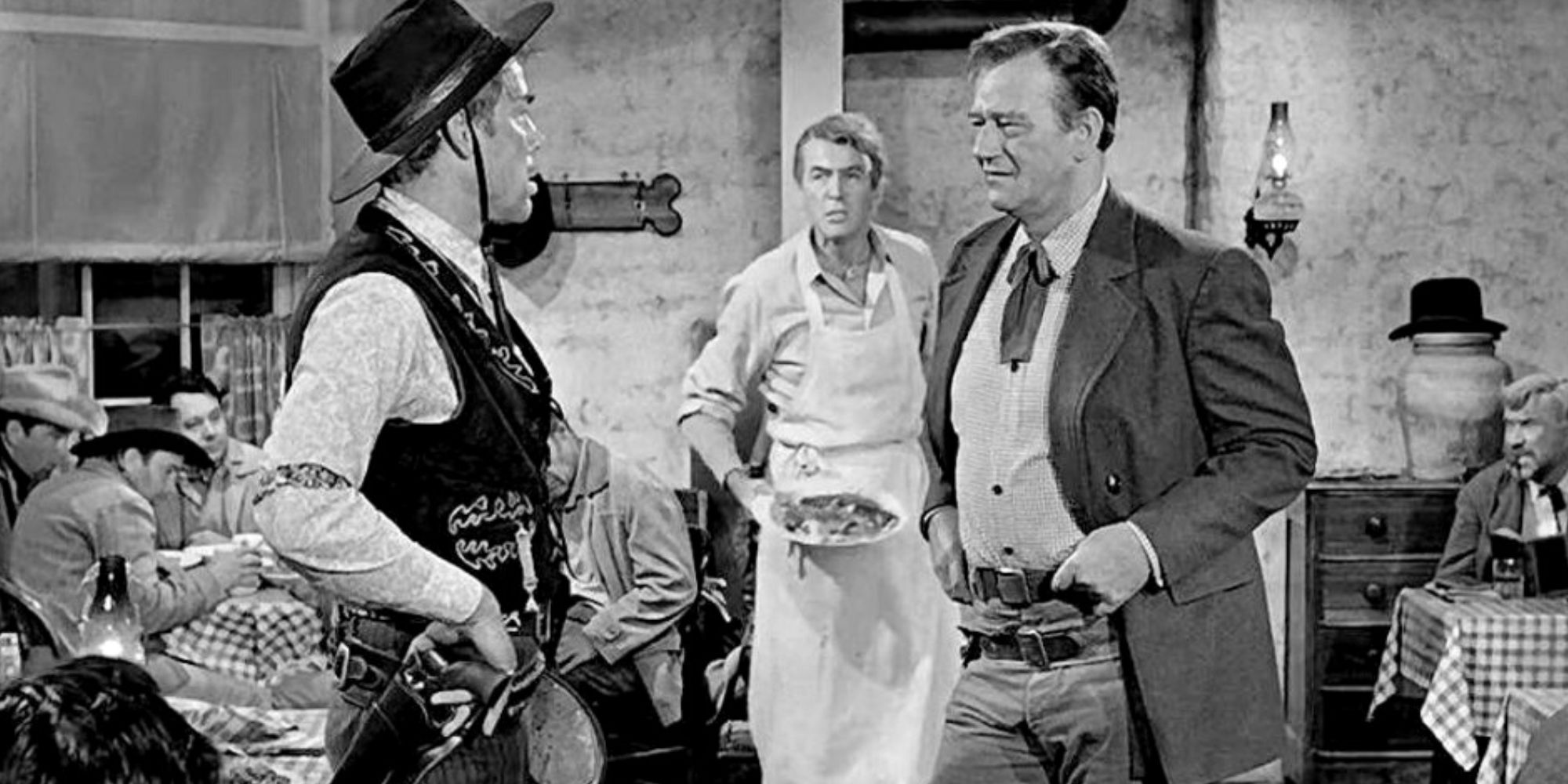 Lee Marvin e John Wayne conversando enquanto Jimmy Stewart está atrás deles em The Man Who Shot Liberty Valance
