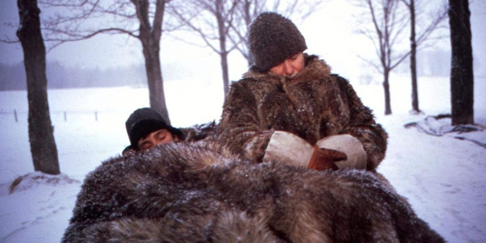 Benoît et l'oncle Antoine assis dans la neige sous des manteaux de fourrure et une couverture dans 