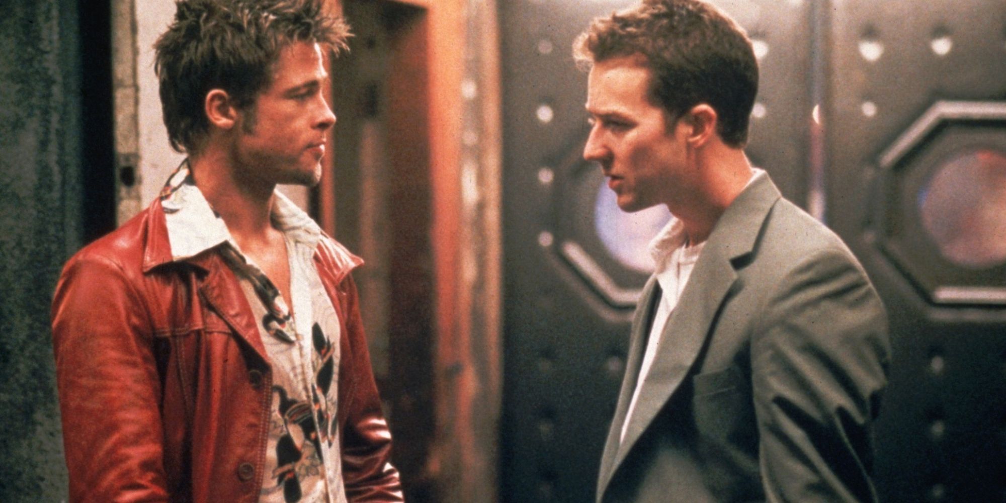 A man in a red leather jacket talks with a man in a grey suit outside a bar.