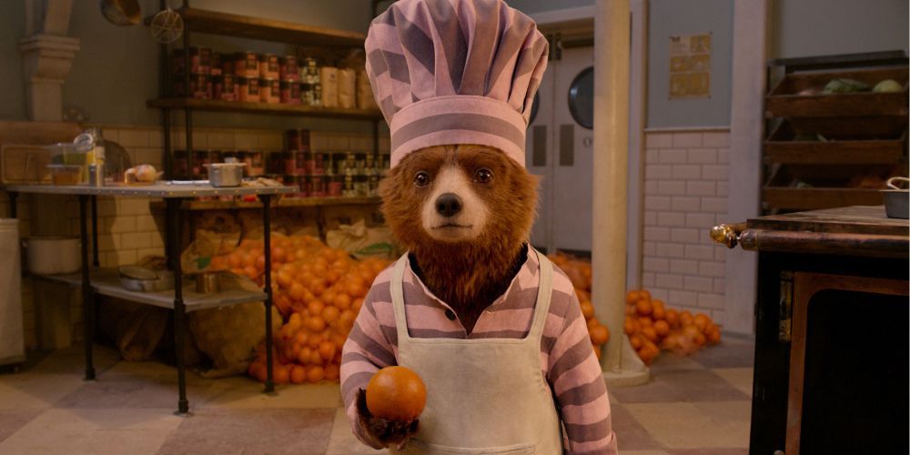 Paddington holding an orange and staring straight ahead in Paddington 2