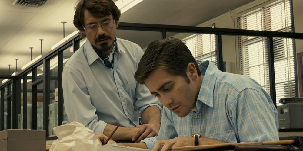 Robert Downey Jr.sitting next to Jake Gyllenhaal watching him write in Zodiac