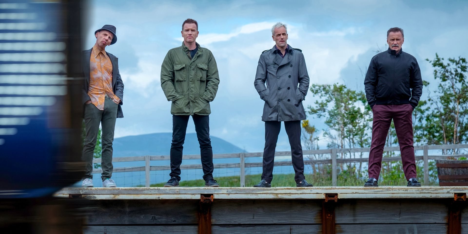 Four old friends stand on a train platform.