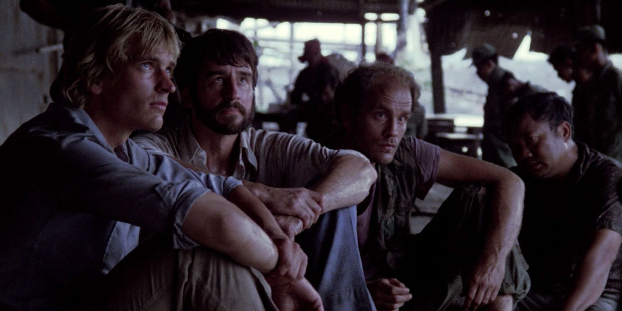 A group of men sitting together and looking up in 'The Killing Fields'