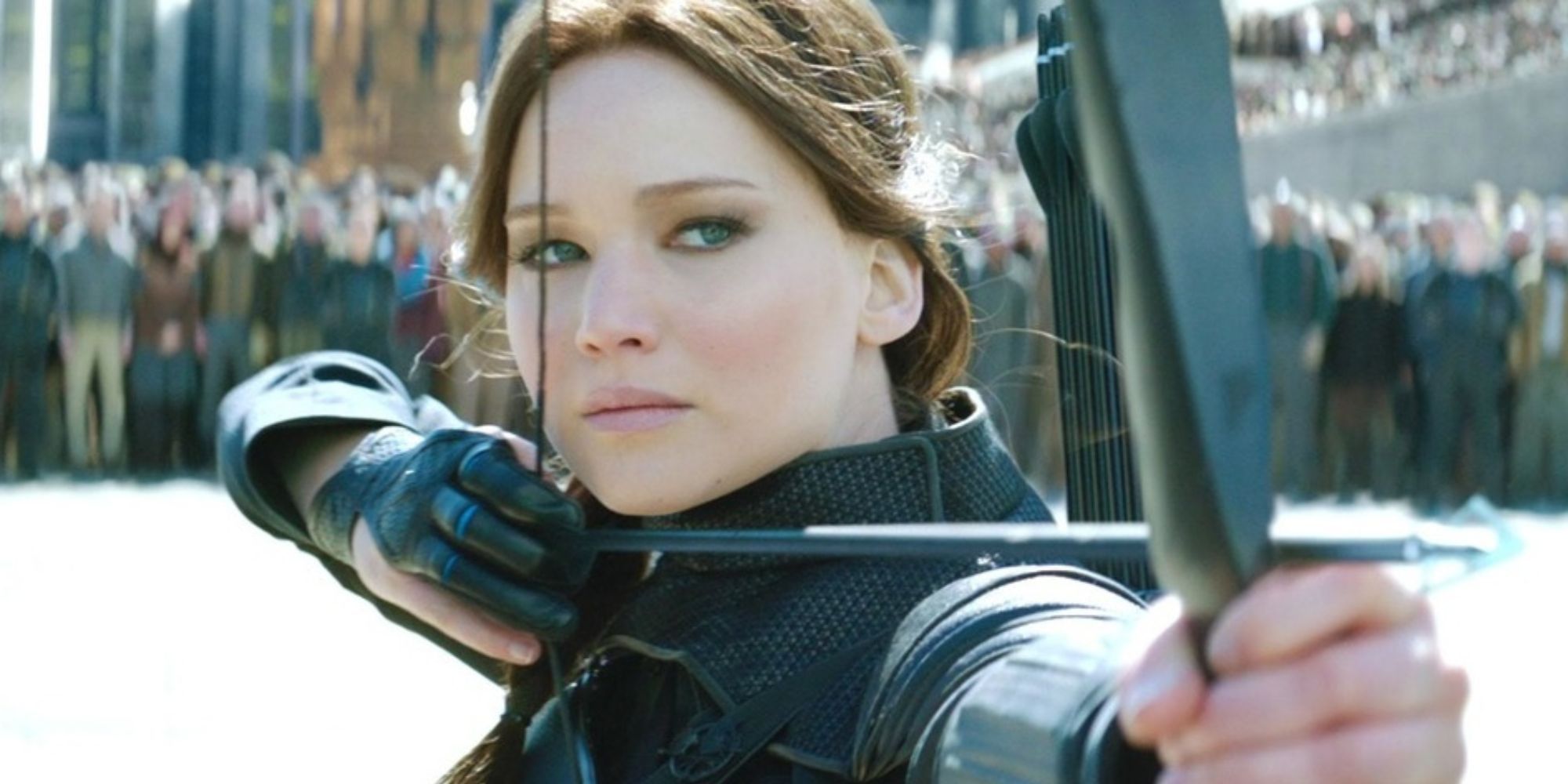 Katniss Everdeen aiming her bow and arrow at something off-camera in 'The Hunger Games'