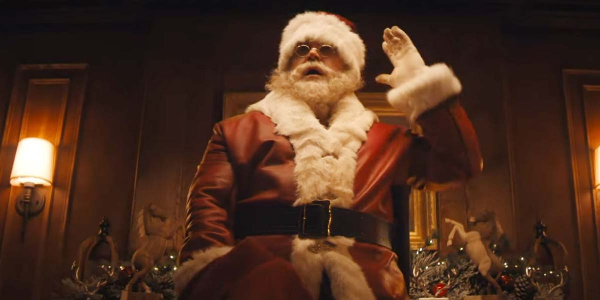 Santa wears a red leather jacket and stands in a home with a Christmas tree in the background in Violent Night.