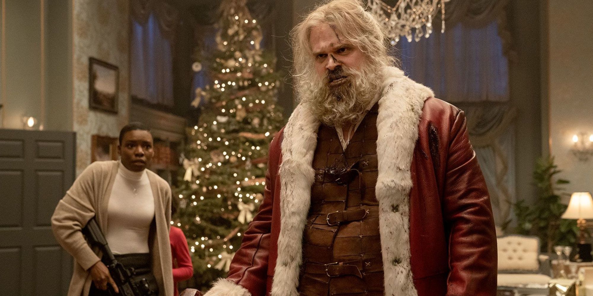 David Harbour as a bloodied Santa holding a mallet with an armed mercenary watching on in fear