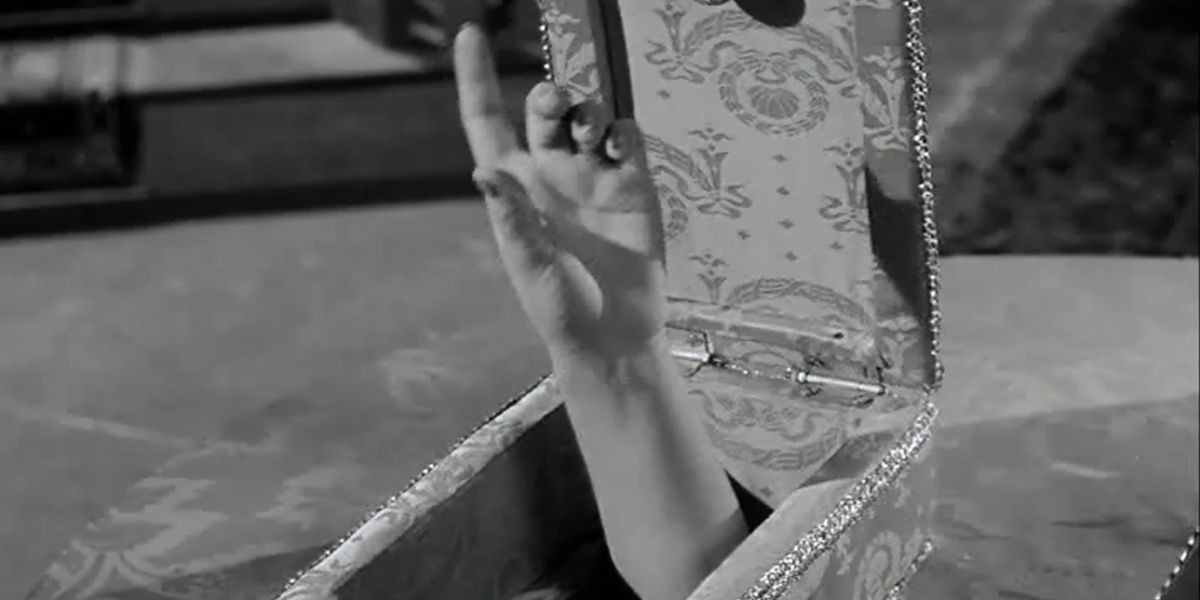 Uma captura de tela em preto e branco da mão/braço de Lady Finger em uma caixa, apresentada na série original Família Addams