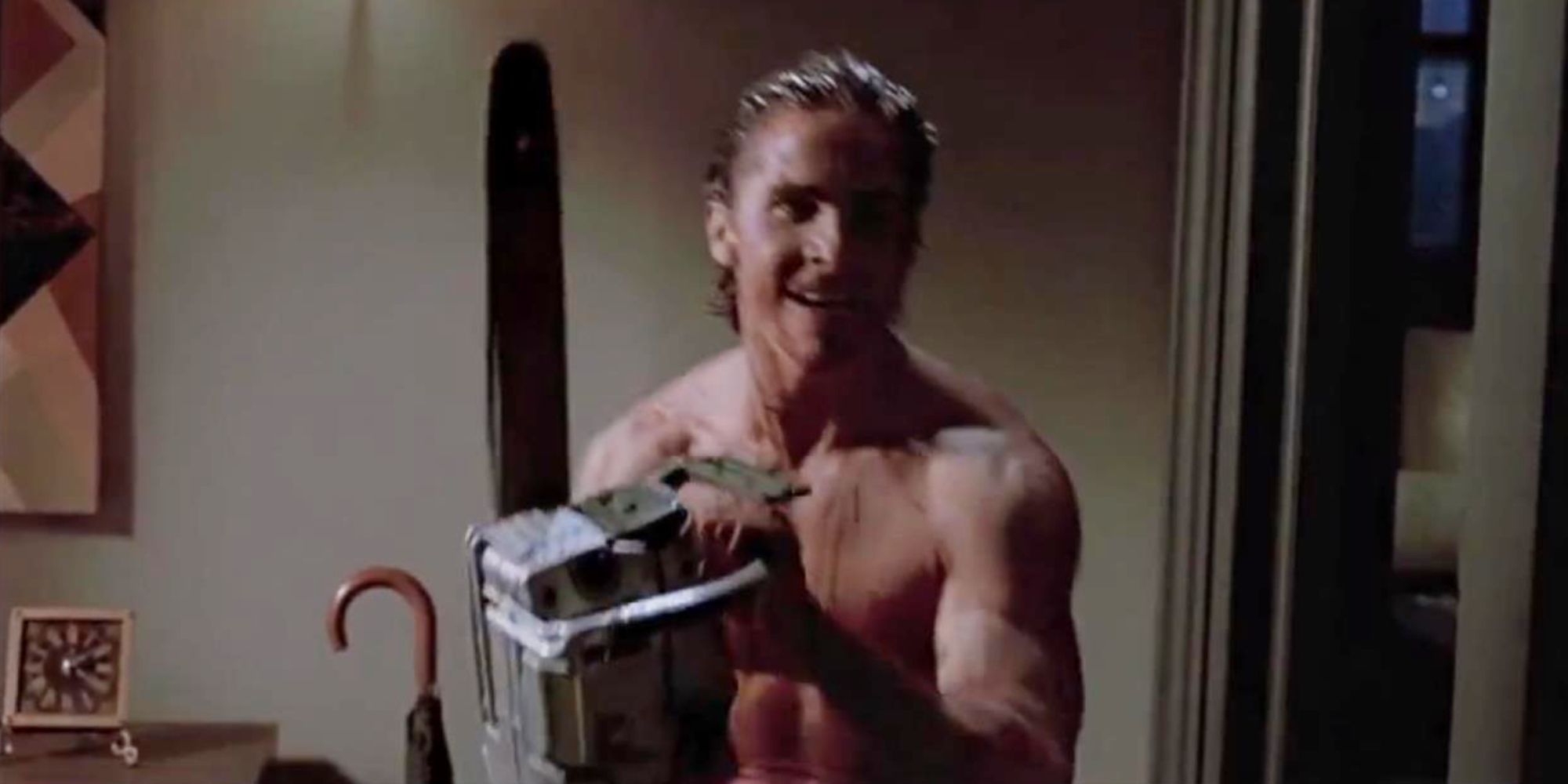 Christian Bale as Patrick Bateman smiling and holding up a chainsaw in American Psycho