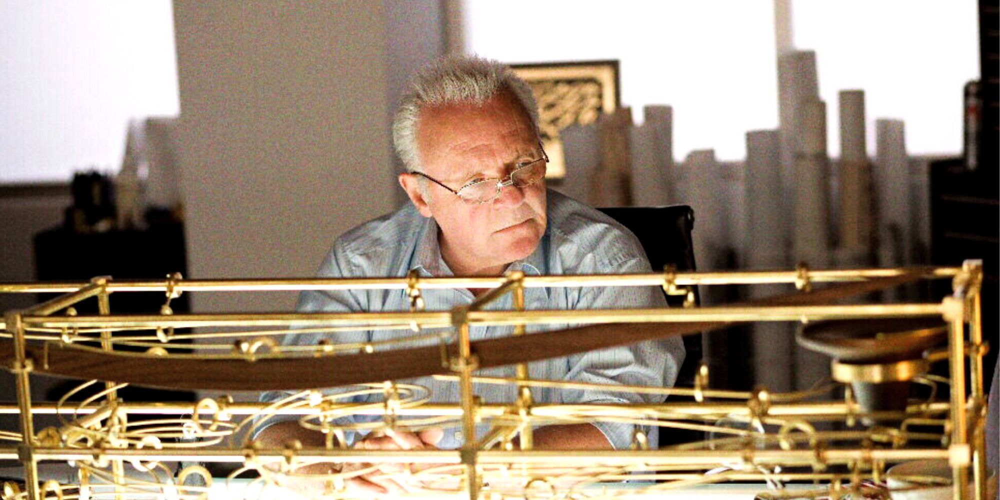 Anthony Hopkins duduk sendirian di meja di depan struktur emas di Fracture