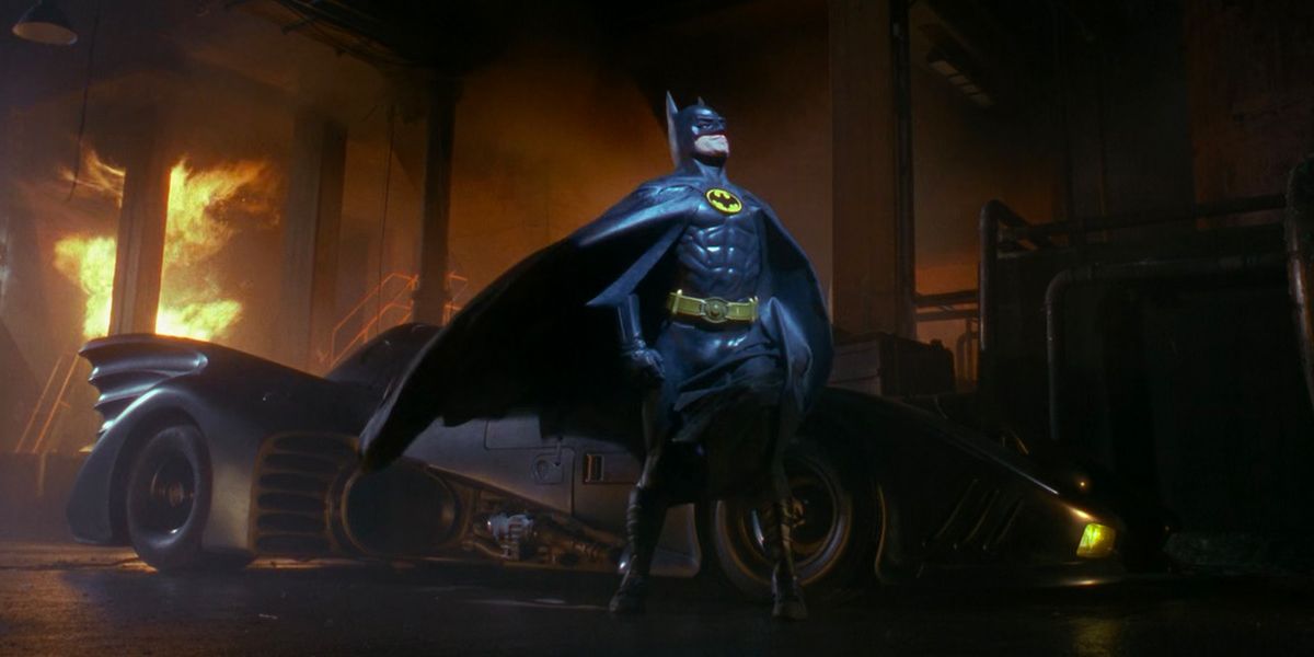 Michael Keaton as Batman in front of the Batmobile