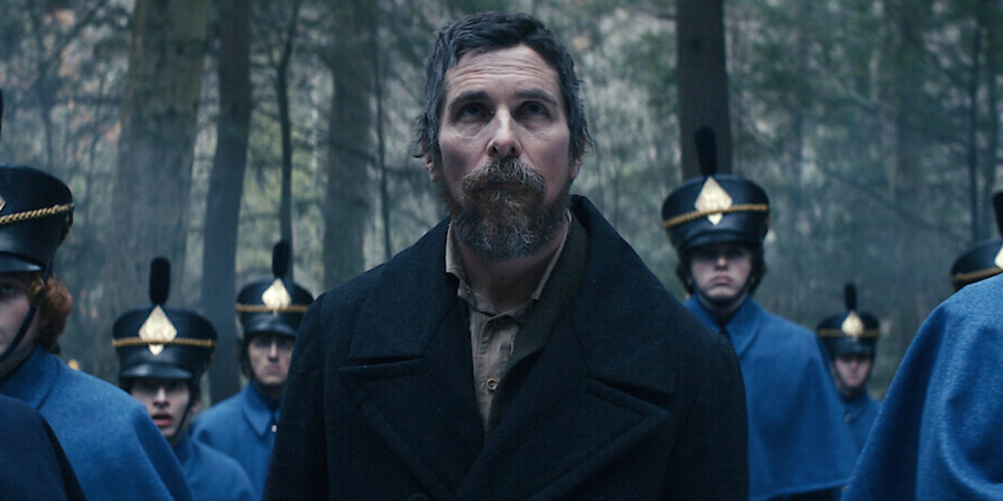 Christian Bale looking up at something with cadets around him in the woods in The Pale Blue Eye