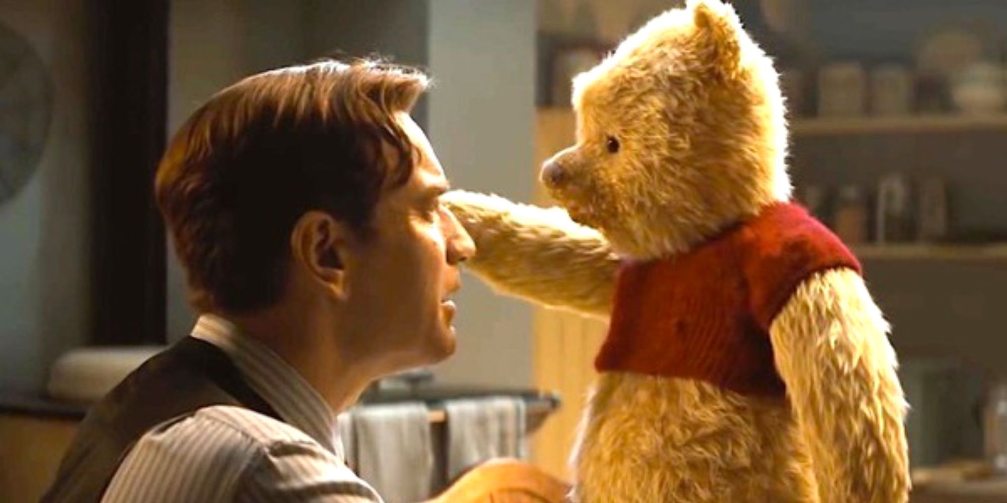 Ewan McGregor talking to Winnie the Pooh who is standing on a table with his arm out in Christopher Robin movie