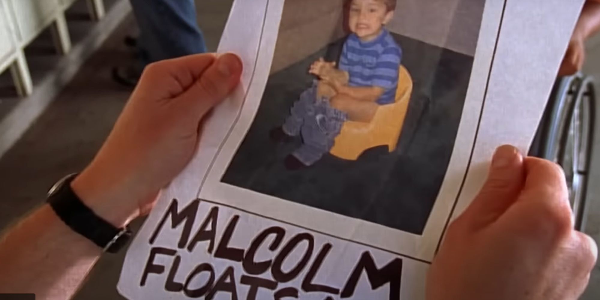 Malcolm segura um livro com uma foto dele quando criança, sentado no banheiro de treinamento, com as palavras 'Malcolm flutua uma ovelha' escritas embaixo dele