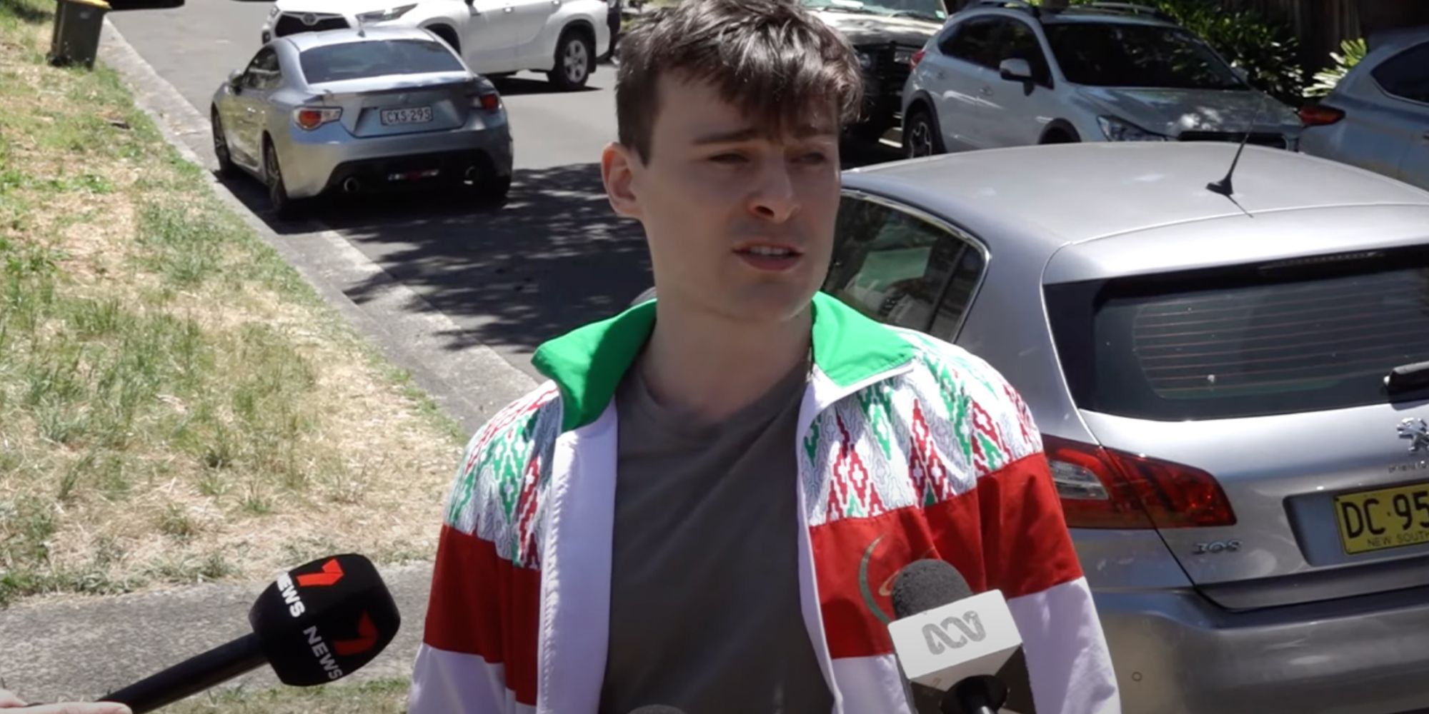 A man being interviewed in his neighborhood with his car behind him
