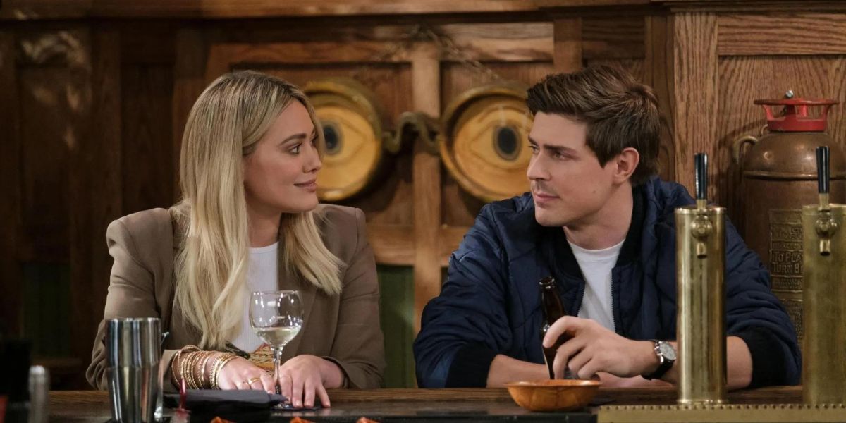 Sophie, played by Hilary Duff, looks over and smiles at Jesse, played by Chris Lowell, as they sit at the bar together in 'How I Met Your Father' Season 1.