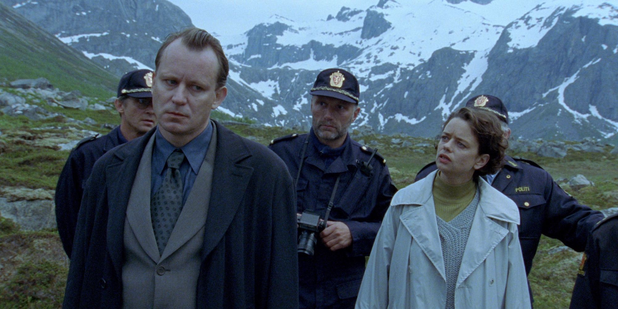 A detective, and several police stand at a crime scene in the mountains 