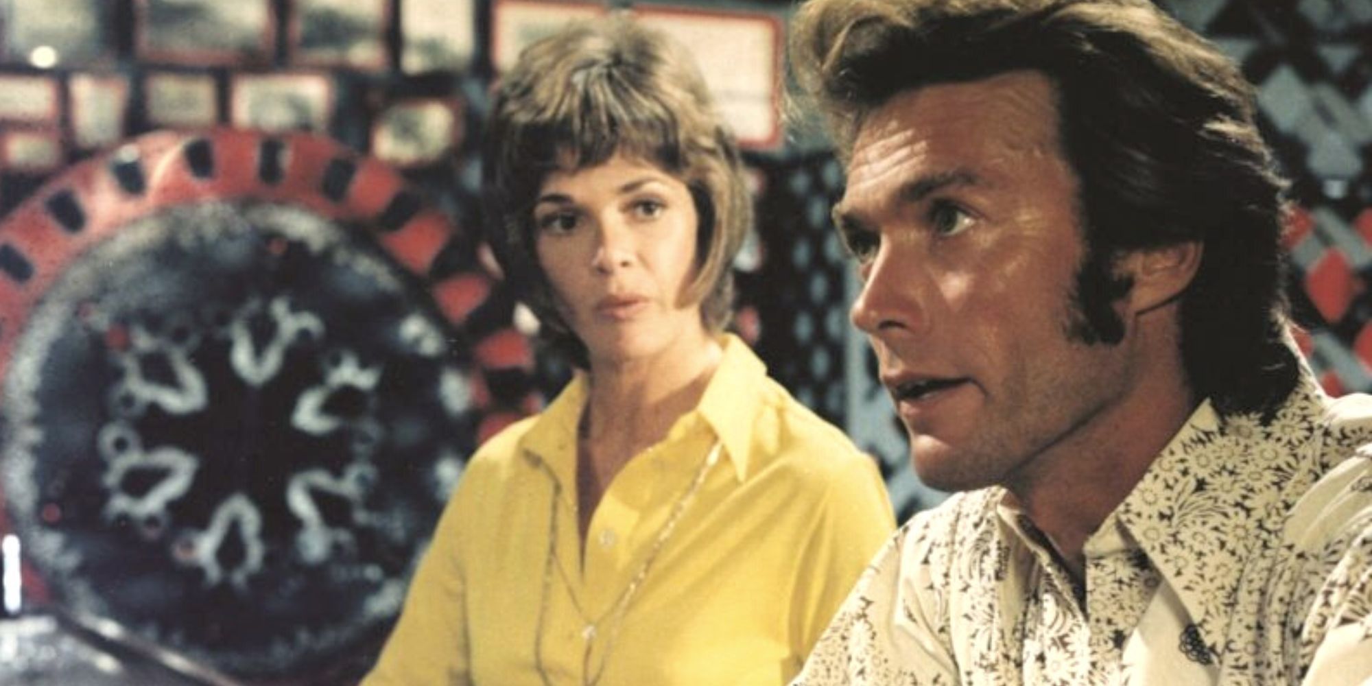 Clint Eastwood looking forward at someone while sitting at a bar with Jessica Walker behind him in Play Misty for Me