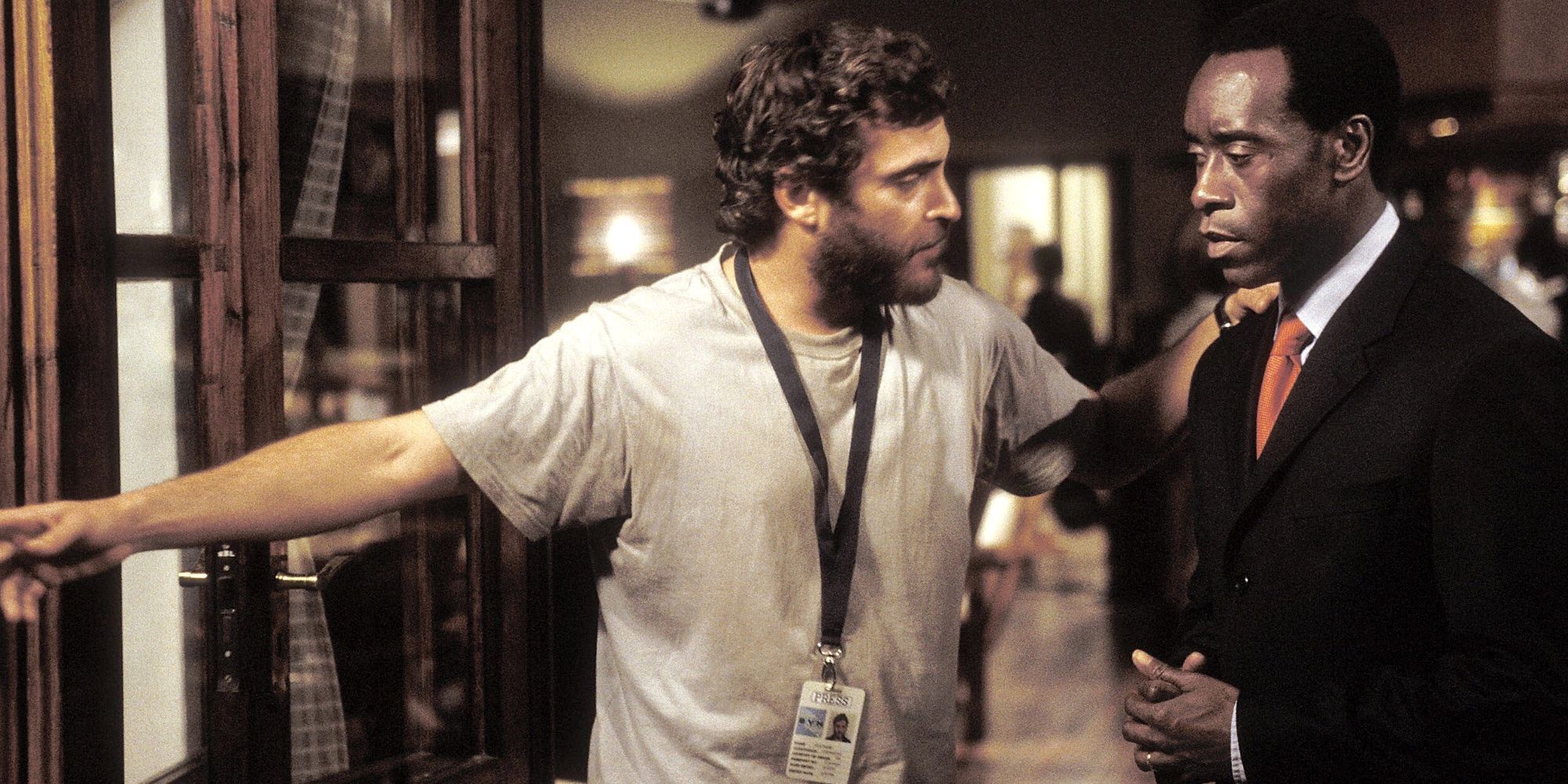 Joaquin Phoenix berdiri di samping Don Cheadle dan mengarahkannya ke depan dengan tangan lainnya di bahunya di Hotel Rwanda