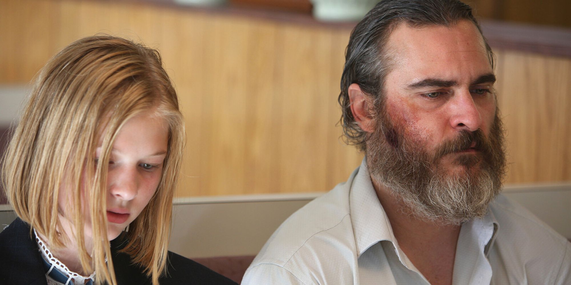 Joaquin Phoenix looking forward while sitting next to Ekaterina Samson who is looking down in You Were Never Really Here