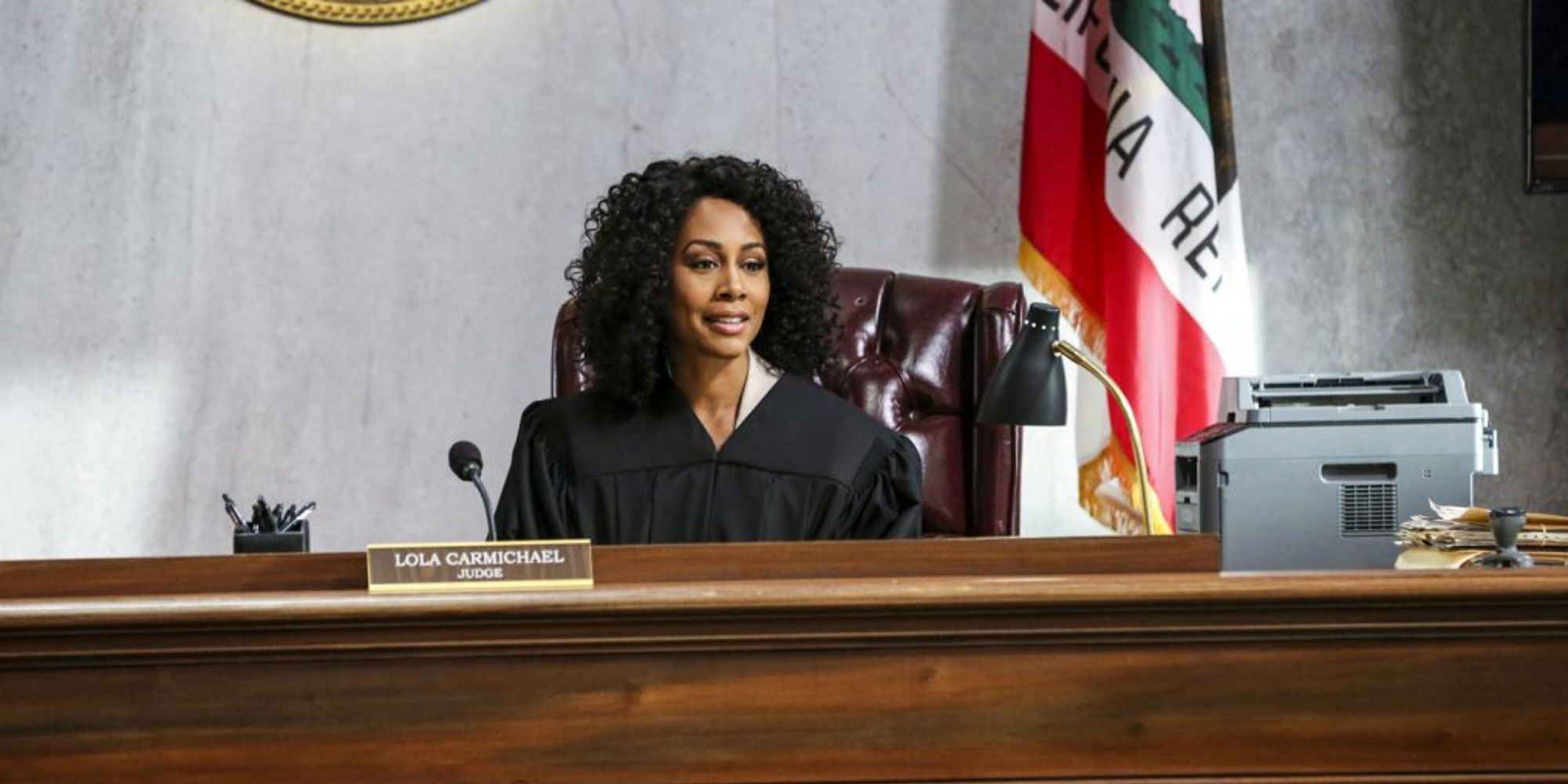 Simone Missick as Judge Lola Carmichael sits at the bench in a courtroom with a flag behind in All Rise.