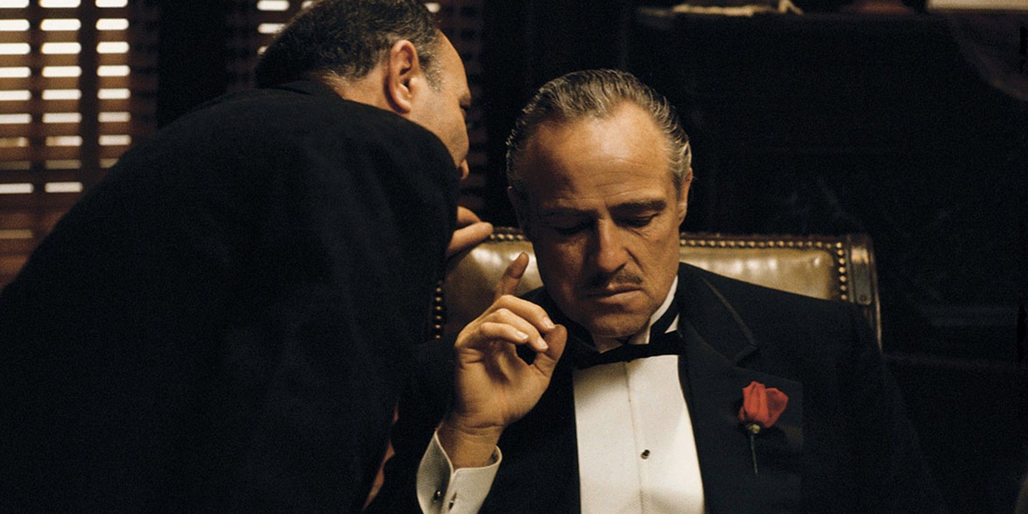 Un homme chuchote quelque chose à l'oreille de Don Vito Corleone dans 'Le Parrain'.