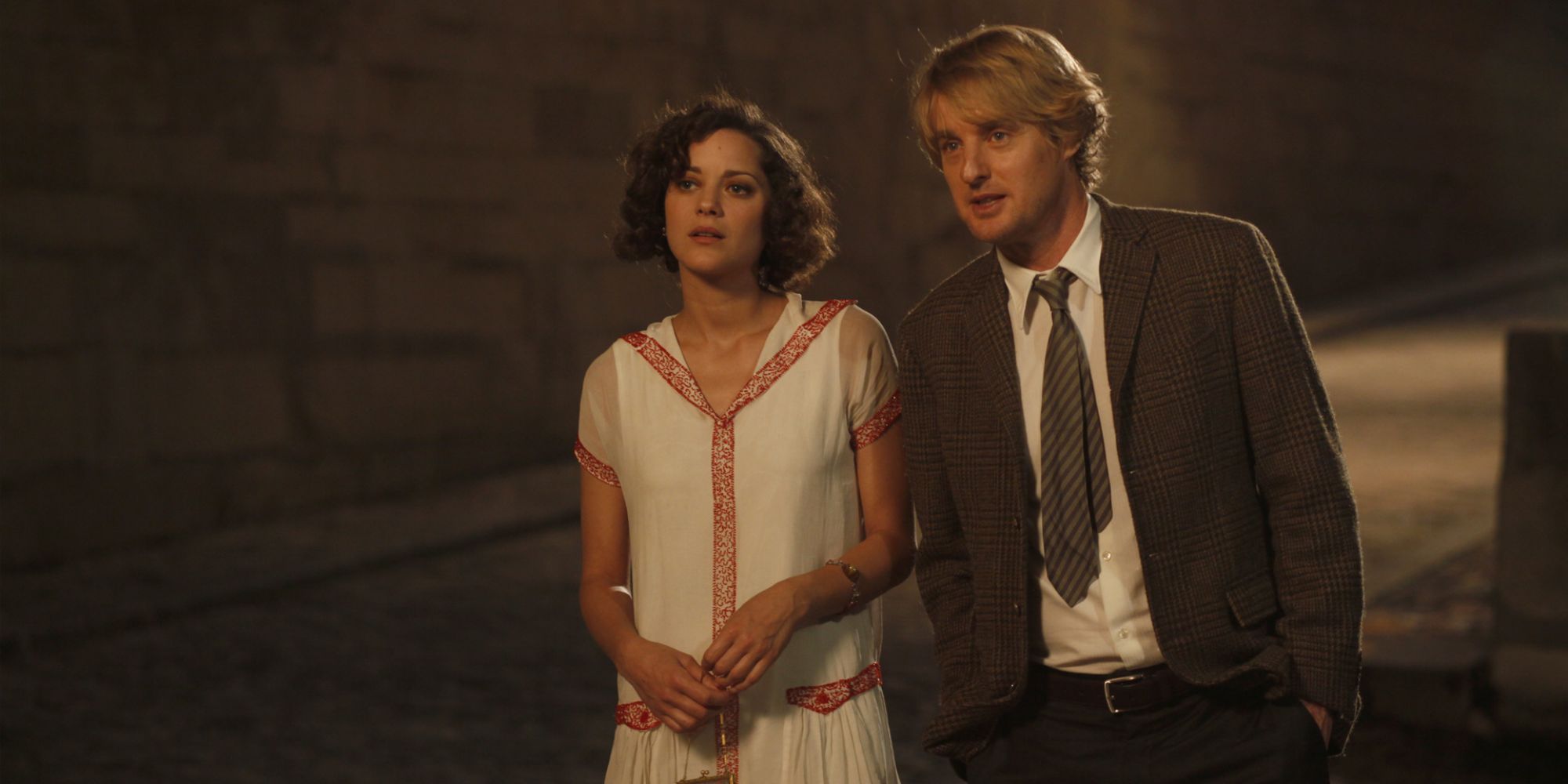 Marion Cotillard and Owen Wilson walk through the streets of Paris together at night.