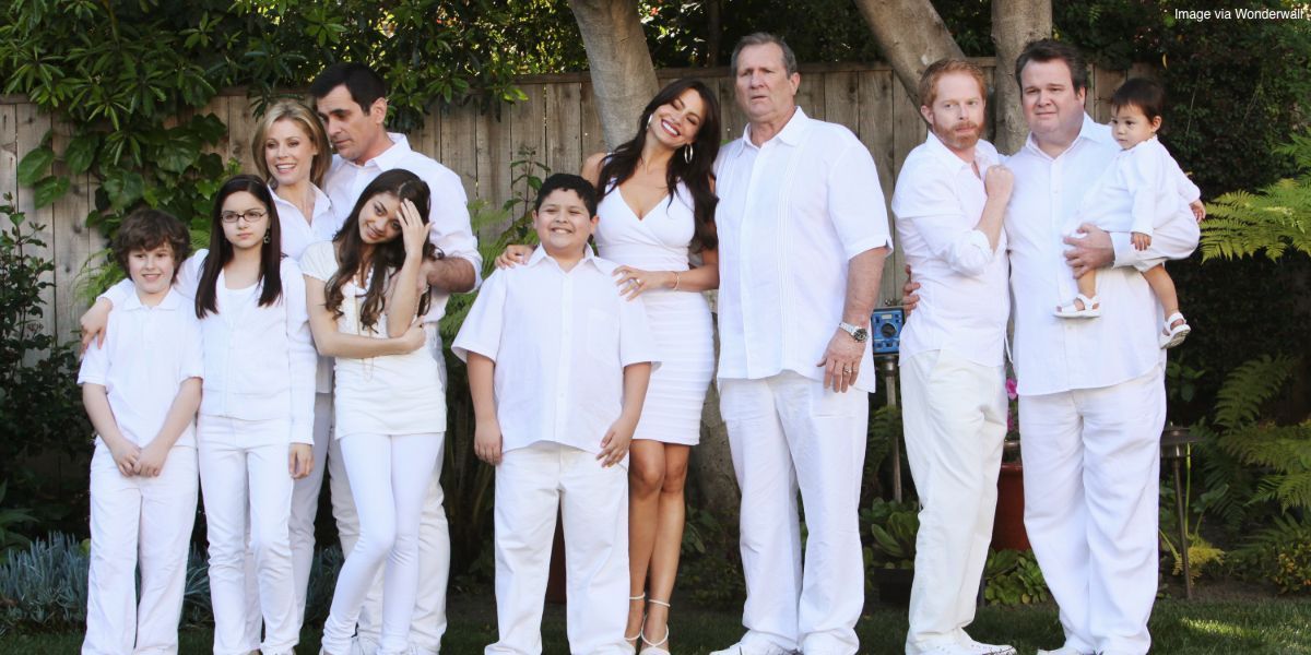 The entire family from Modern Family posing in a backyard, everyone wearing white.