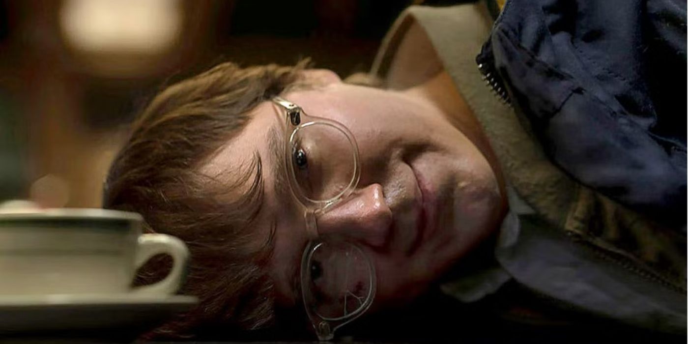 The Riddler, played by Paul Dano, smiling with his head down against the counter during the arrest scene in 'The Batman.'