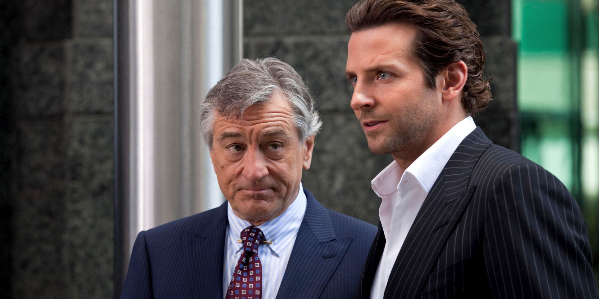 Robert De Niro looking at Bradley Cooper standing next to him while looking at something ahead in Limitless