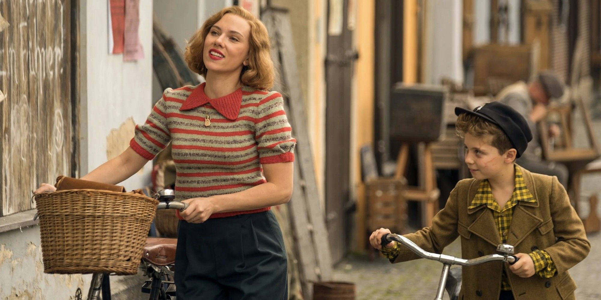 Roman Griffin Davis, que interpreta a Jojo, y Scarlett Johansson, que interpreta a su madre en Jojo Rabbit, andan en bicicleta por la calle.